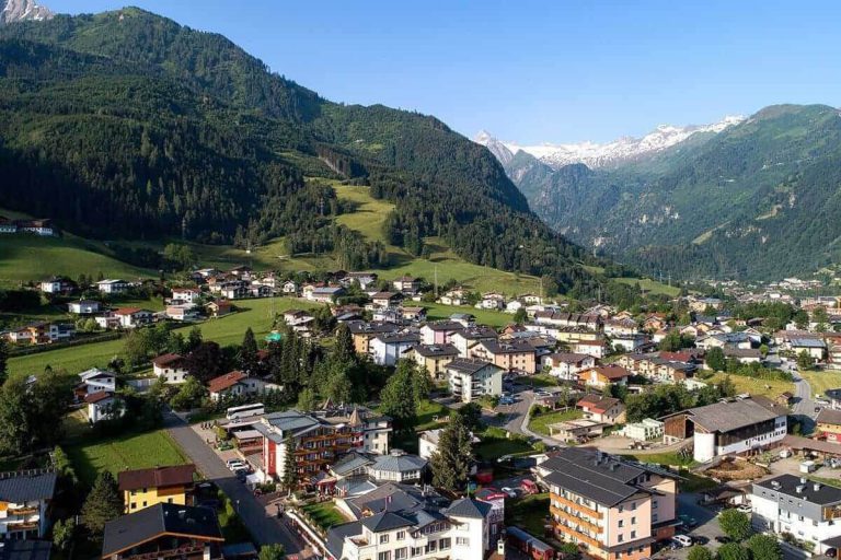 Blick auf Kaprun mit Bergen, grünen Wiesen und typischer Architektur. Ideal für Urlaub.