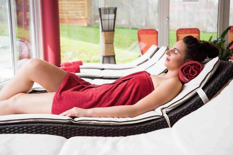 Entspannte Frau im Wellnessbereich mit rotem Handtuch und Blick ins Grüne.